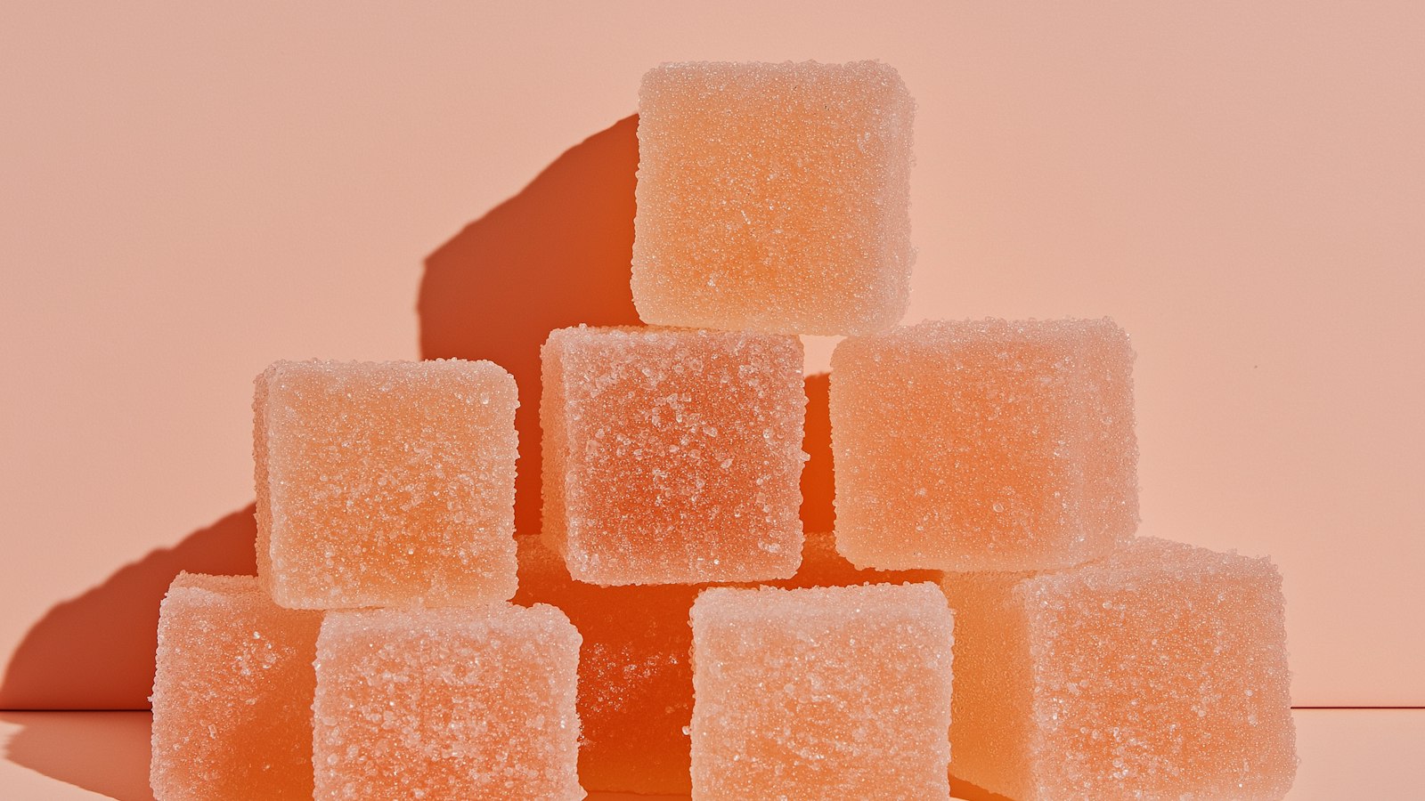 Stacked sugar-coated orange gummy cubes against a peach-colored background