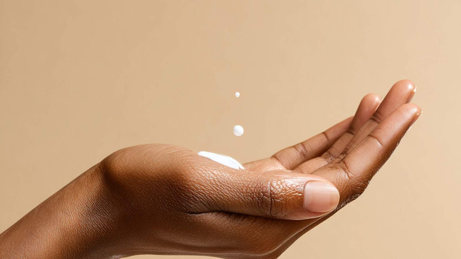 Open palm holding a dab of white moisturizing cream against a beige background